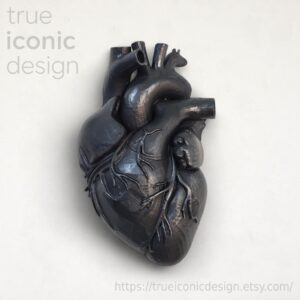 Scultura di cuore anatomico grigio scuro con dettagli intricati delle vene. La scultura ha una finitura metallica ed è posta su uno sfondo bianco. Il testo "true iconic design" è visibile in alto a sinistra.